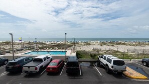 Un parking rempli de véhicules, une piscine et, au loin, une plage.