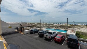 A parking area with several vehicles, a pool, and a beach view. - Island Winds East 109 2 Bedroom Condo (Gulf Shores)