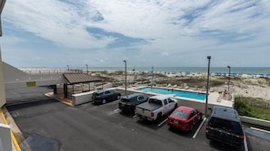 A parking area with several vehicles, a pool, and a beach view. - Island Winds East 109 2 Bedroom Condo (Gulf Shores)