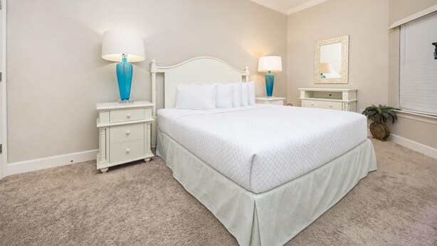A bedroom with a large bed, two bedside tables, a nightstand, a mirror, and a potted plant. - The Oasis 2410 Formerly Phoenix West Ii 2410 3 Bedroom Condo (Orange Beach)
