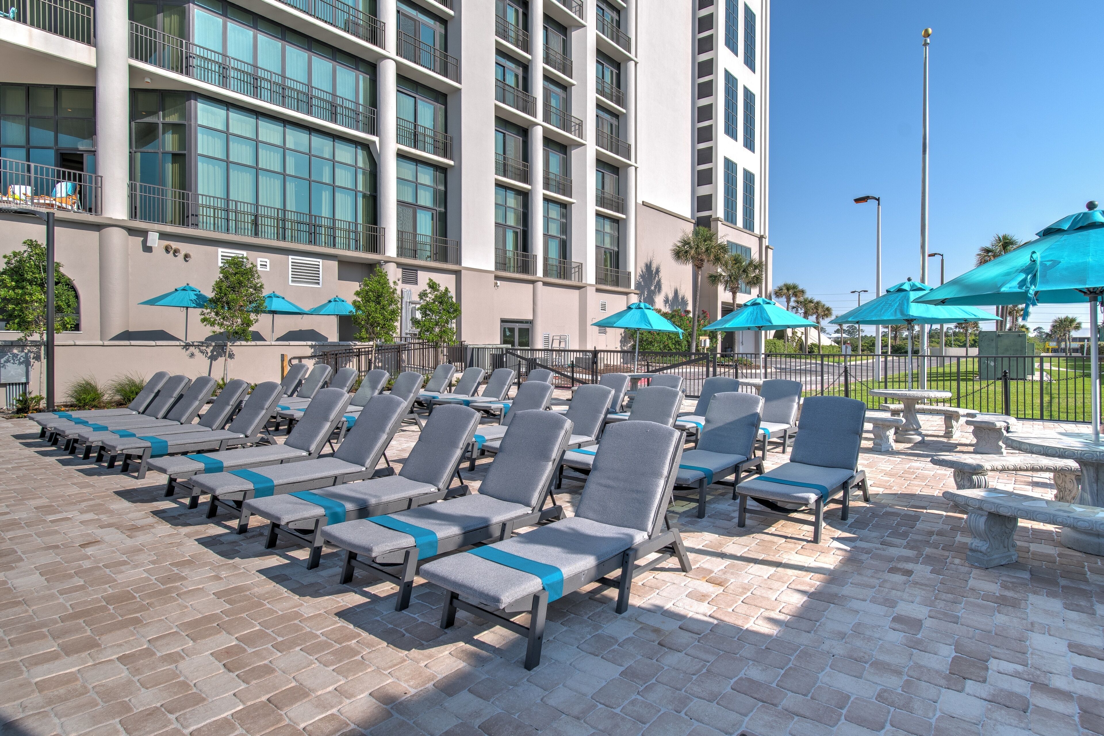 A rooftop pool area with sun loungers and umbrellas, a high-rise building in the background, and a clear sky.
