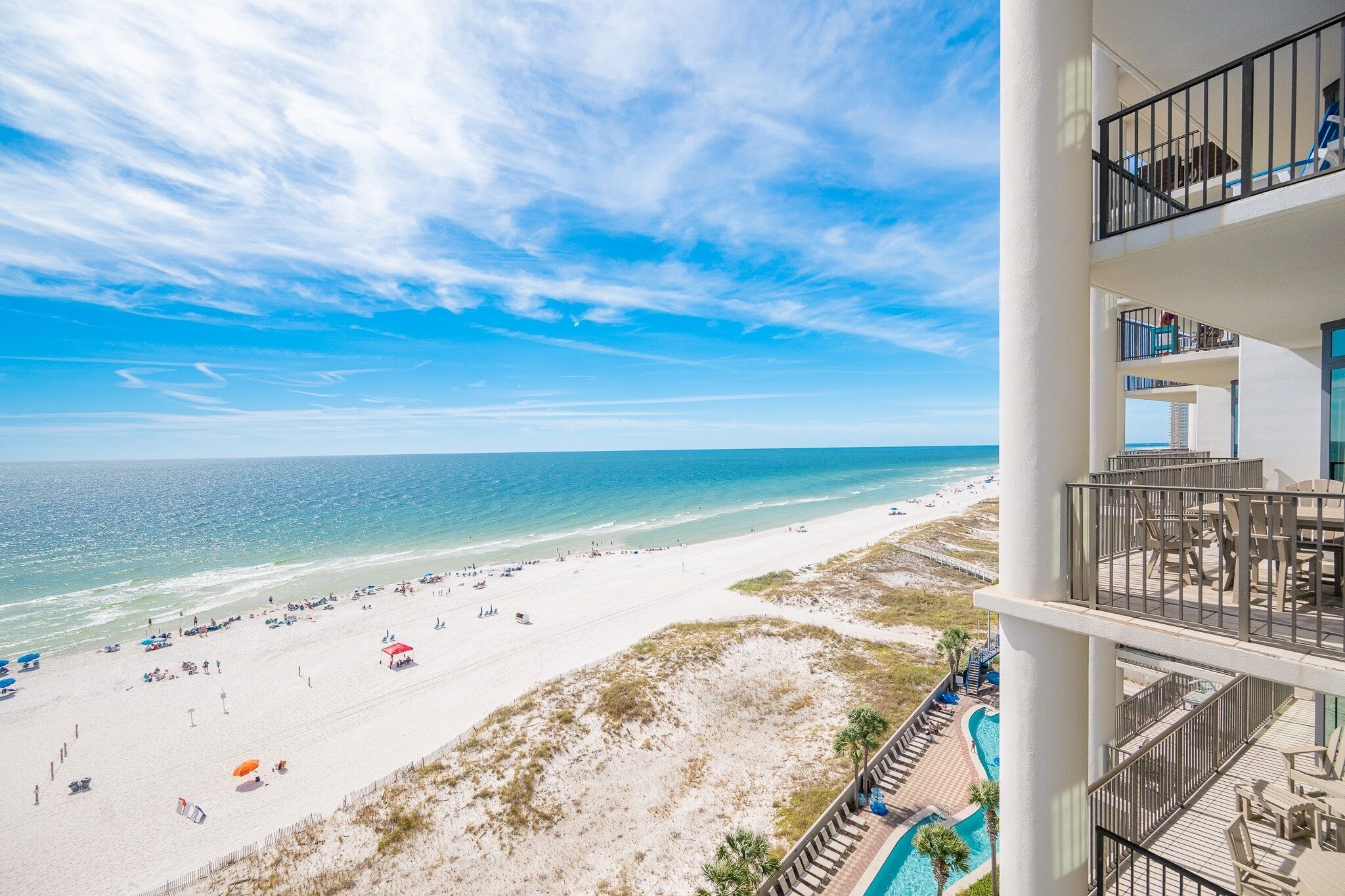A beach view from a balcony with a pool and outdoor seating.