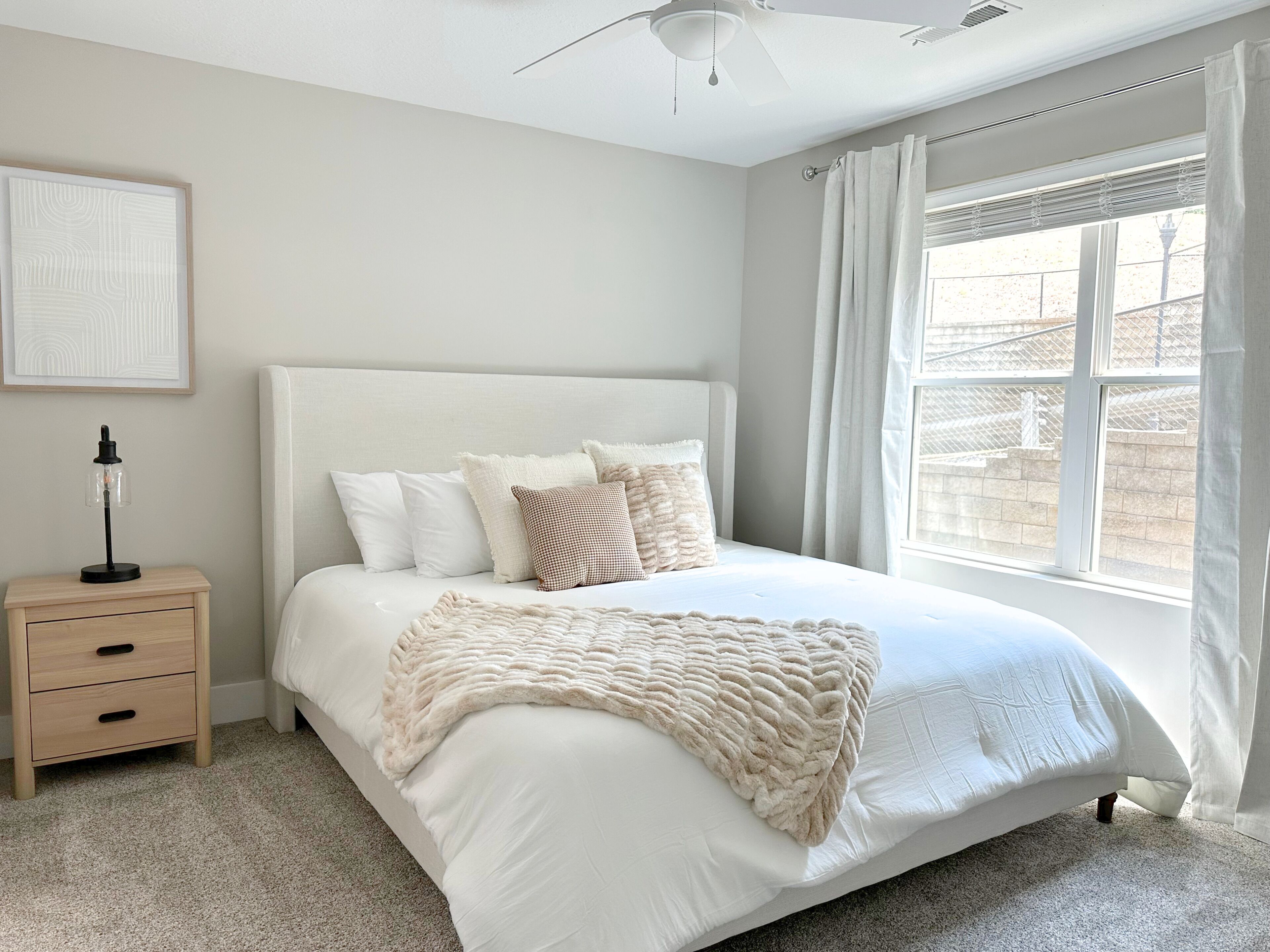 A bedroom with a bed, a nightstand, a ceiling fan, and a window with curtains.