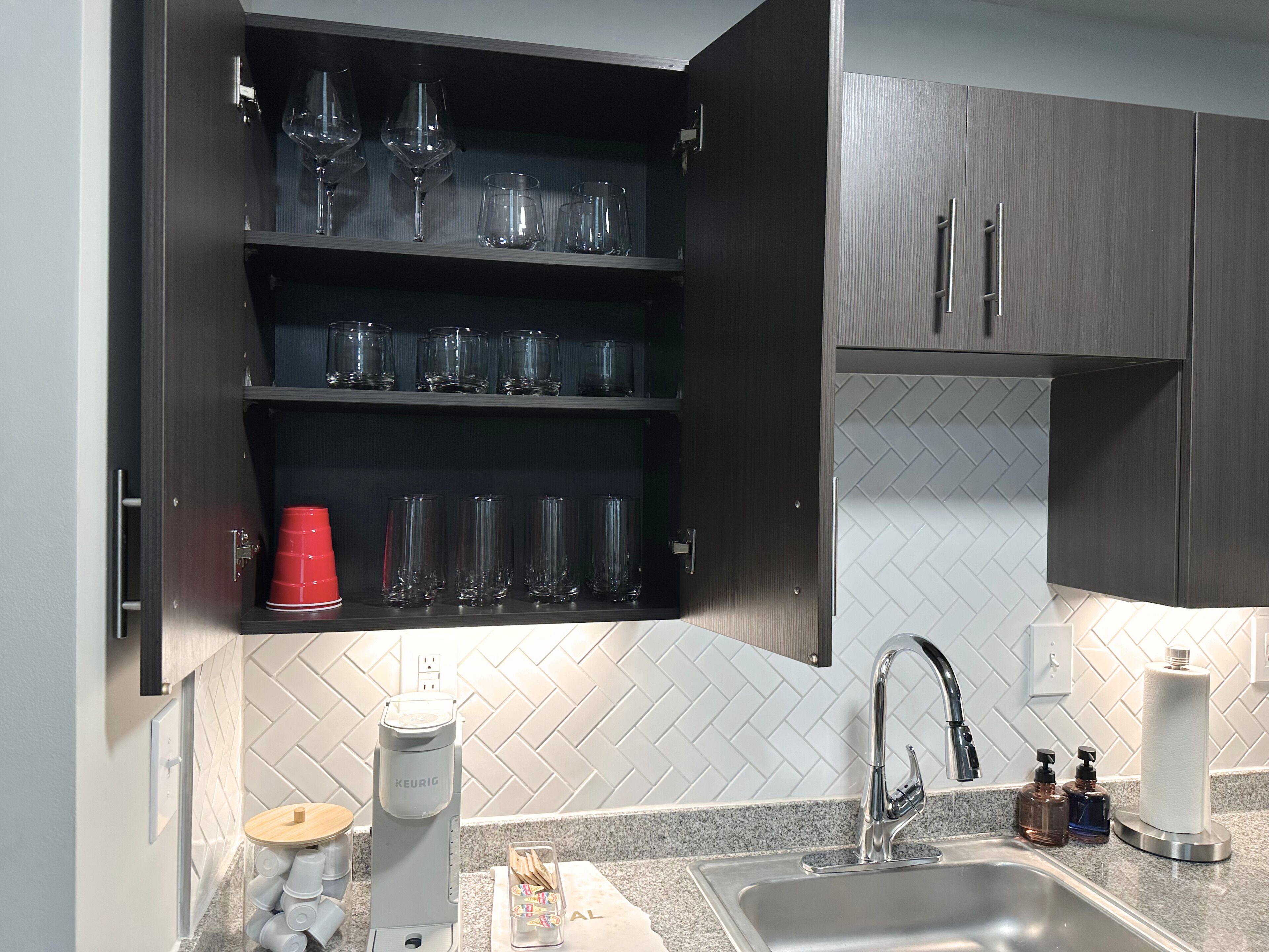 A kitchen with a built-in coffee maker, a sink, and a cabinet with glassware.