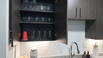 A kitchen with a built-in coffee maker, a sink, and a cabinet with glassware.