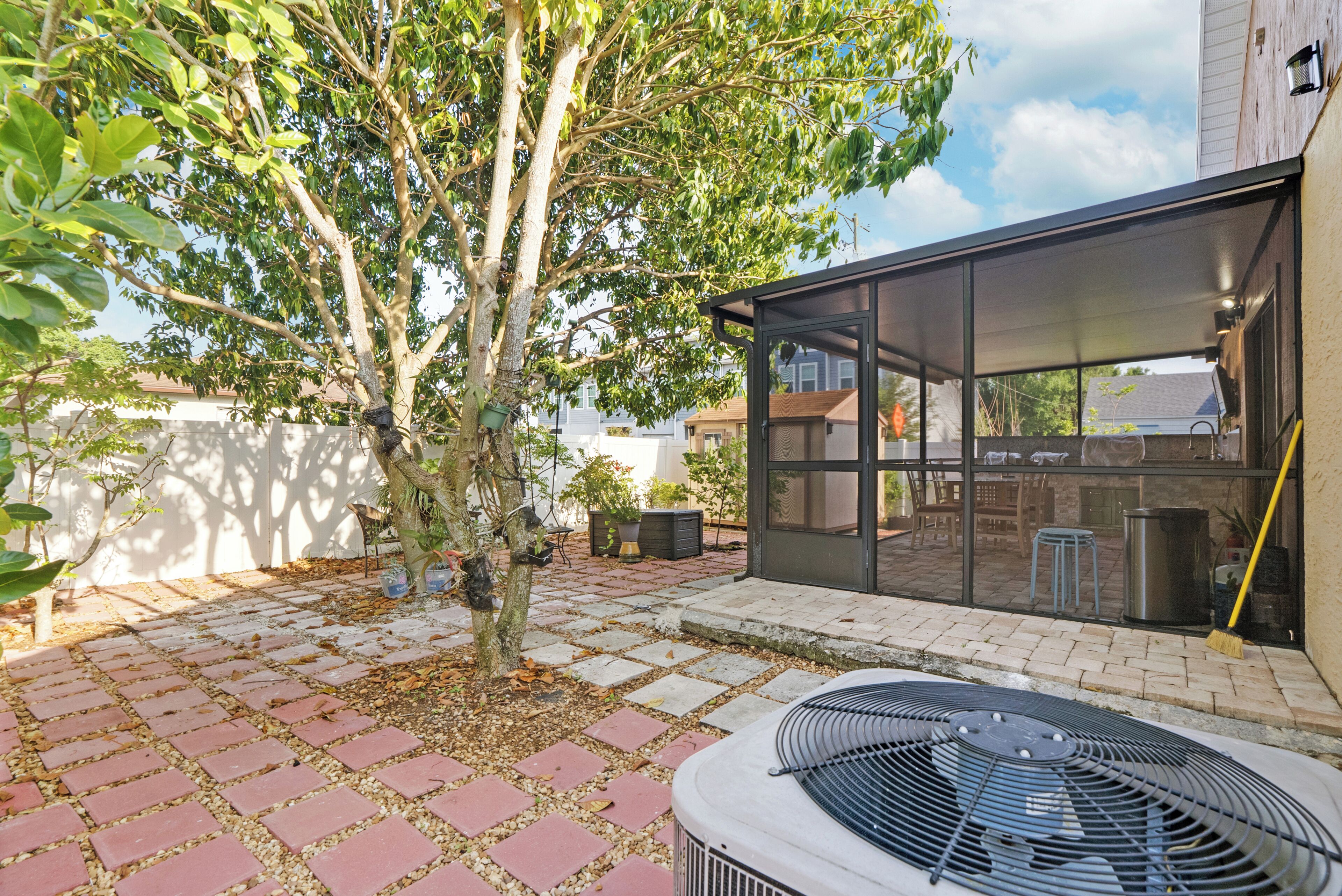 A patio with a grill, a tree, and a glass enclosure.
