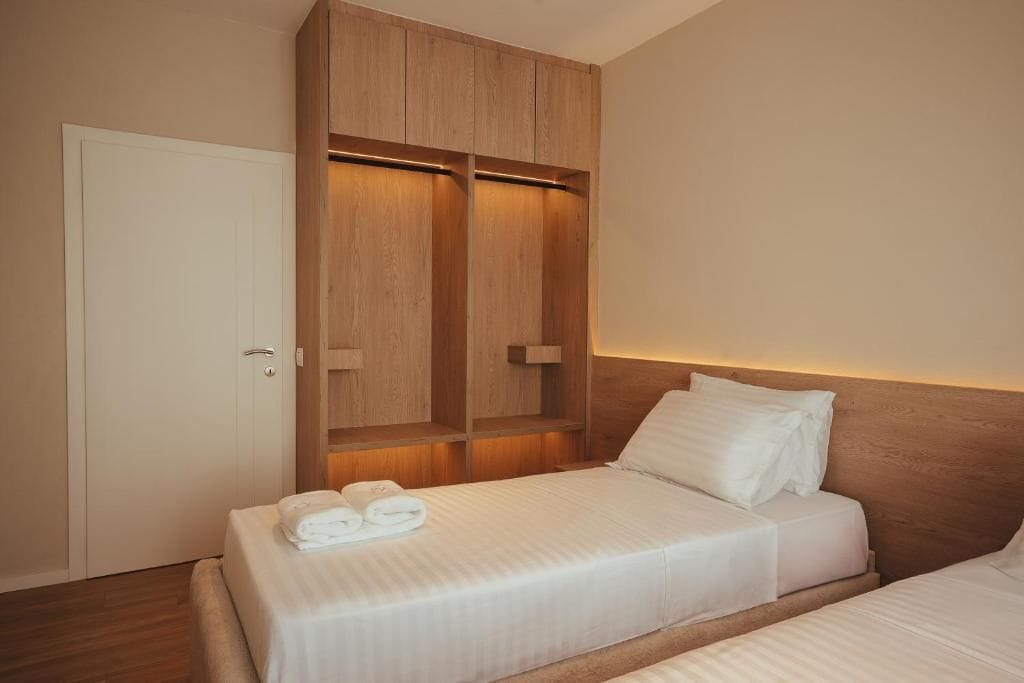 A hotel room with a bed, a wardrobe, and a bedside table.