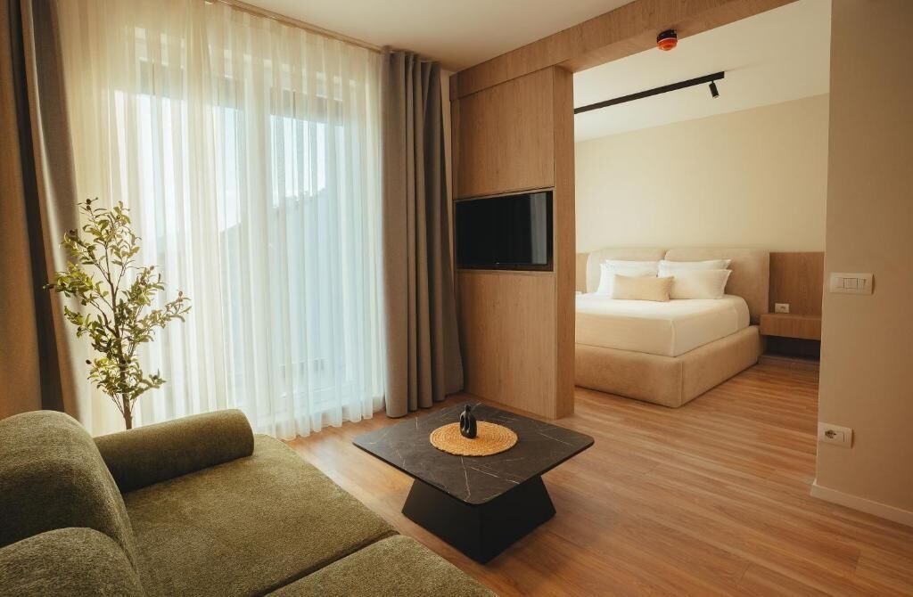 Une chambre d’hôtel moderne, dotée d’un canapé, d’un téléviseur à écran plat fixé au mur, d’un lit avec du linge de maison blanc et d’une petite plante sur le rebord de la fenêtre.
