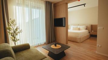 Une chambre d’hôtel moderne, dotée d’un canapé, d’un téléviseur à écran plat fixé au mur, d’un lit avec du linge de maison blanc et d’une petite plante sur le rebord de la fenêtre.
