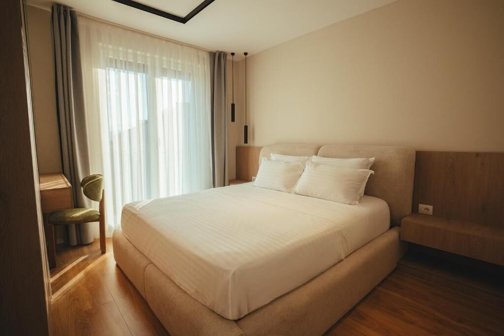 A bedroom with a large bed, a chair, and a window with curtains.