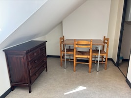 A room with a wooden dresser, a dining table with chairs, and a sloped ceiling.