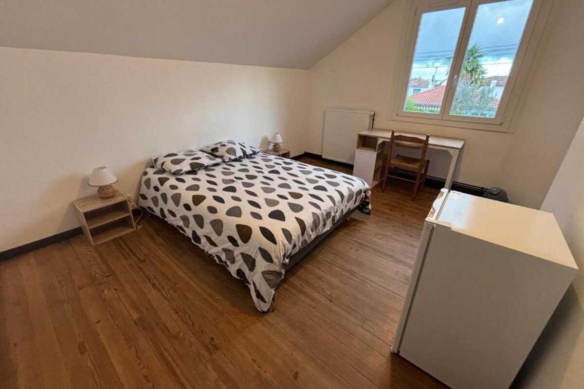 A bedroom with a bed, a desk, a chair, a radiator, and a window with a view.