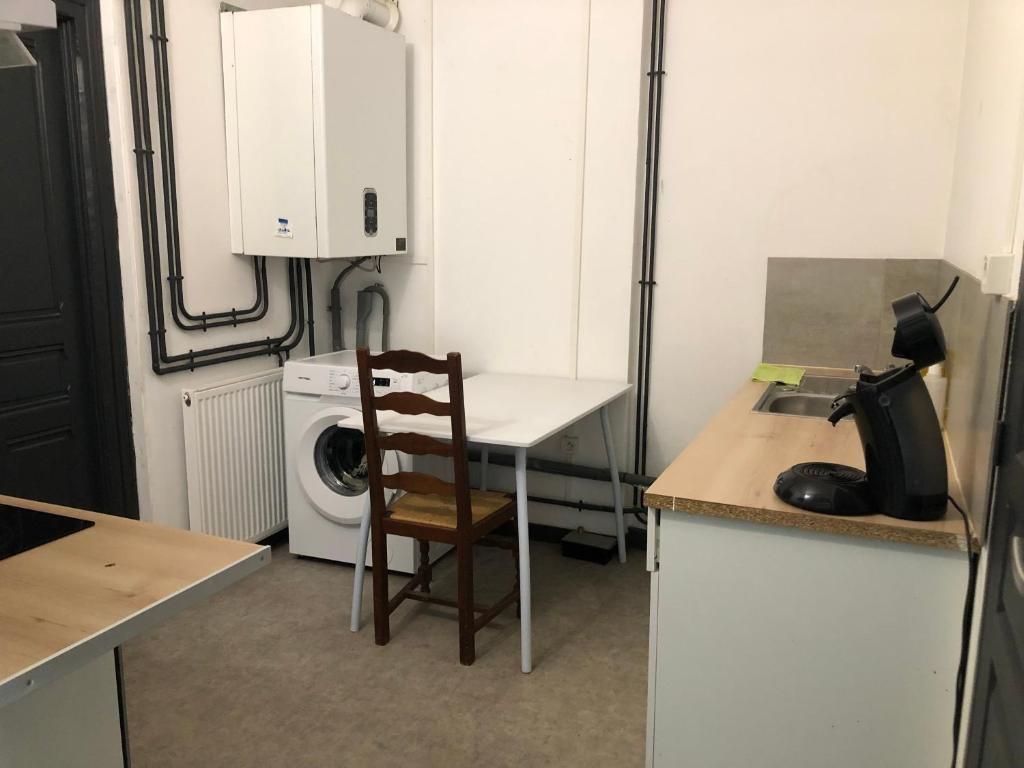 A compact kitchen with a washing machine, a chair, and a small table.