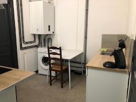 A compact kitchen with a washing machine, a chair, and a small table.