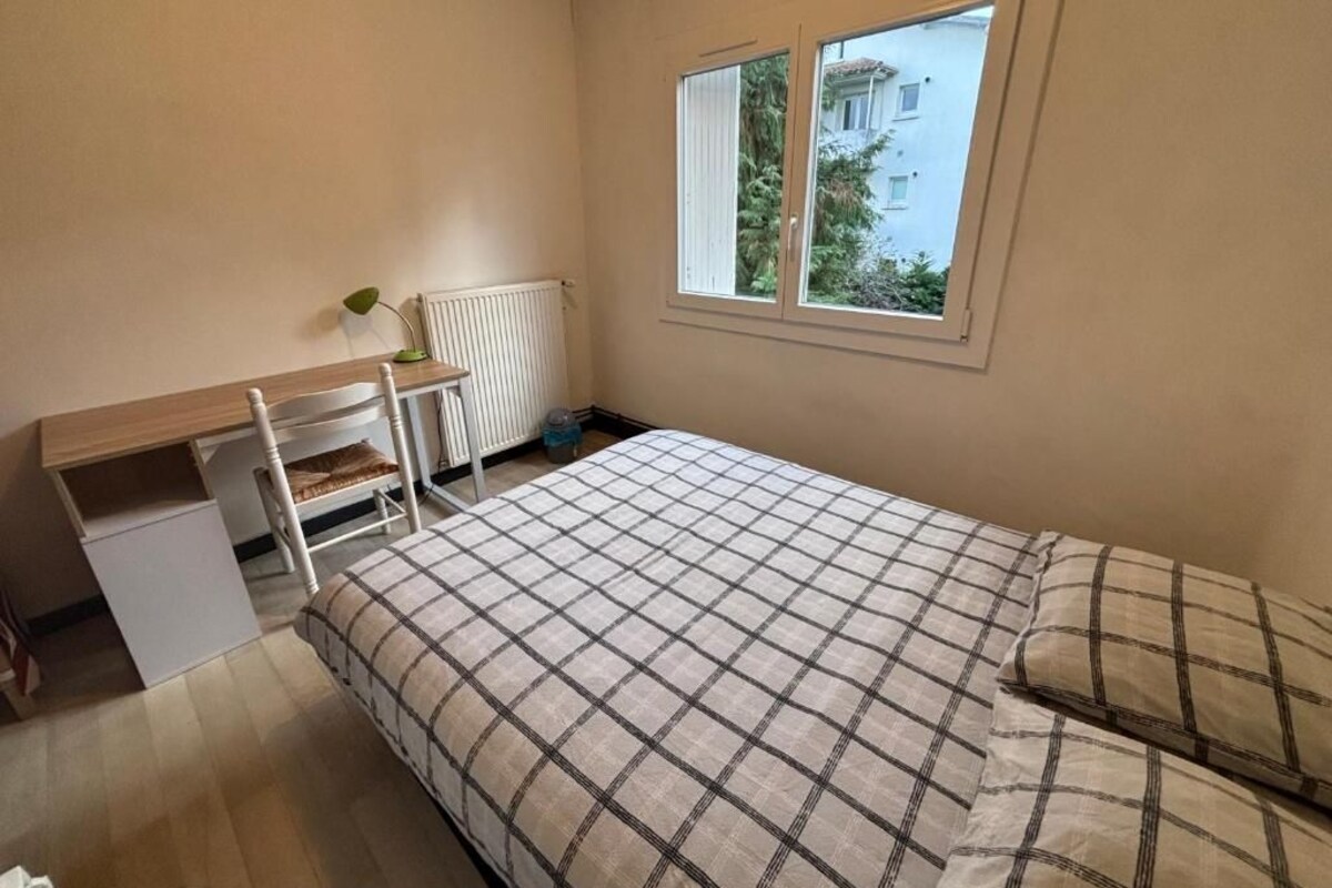 A bedroom with a bed, a desk, a chair, and a window.