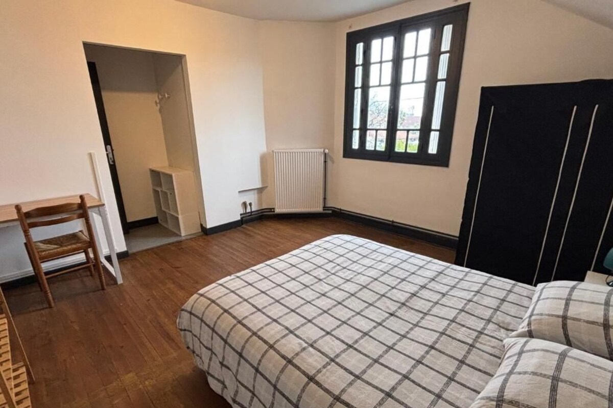 A bedroom with a bed, a chair, a radiator, and a window.