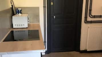 A compact kitchen with a microwave, a small refrigerator, and a black door.