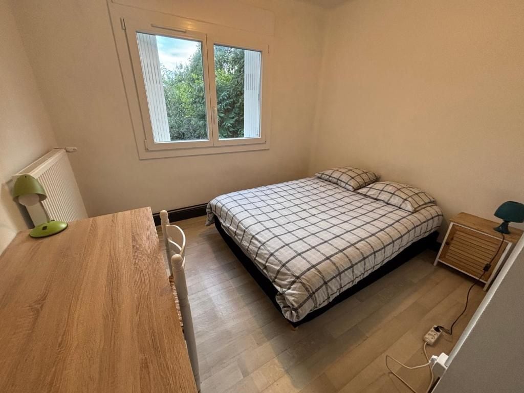 Un dormitorio con una cama, un escritorio de madera, una ventana y un radiador.