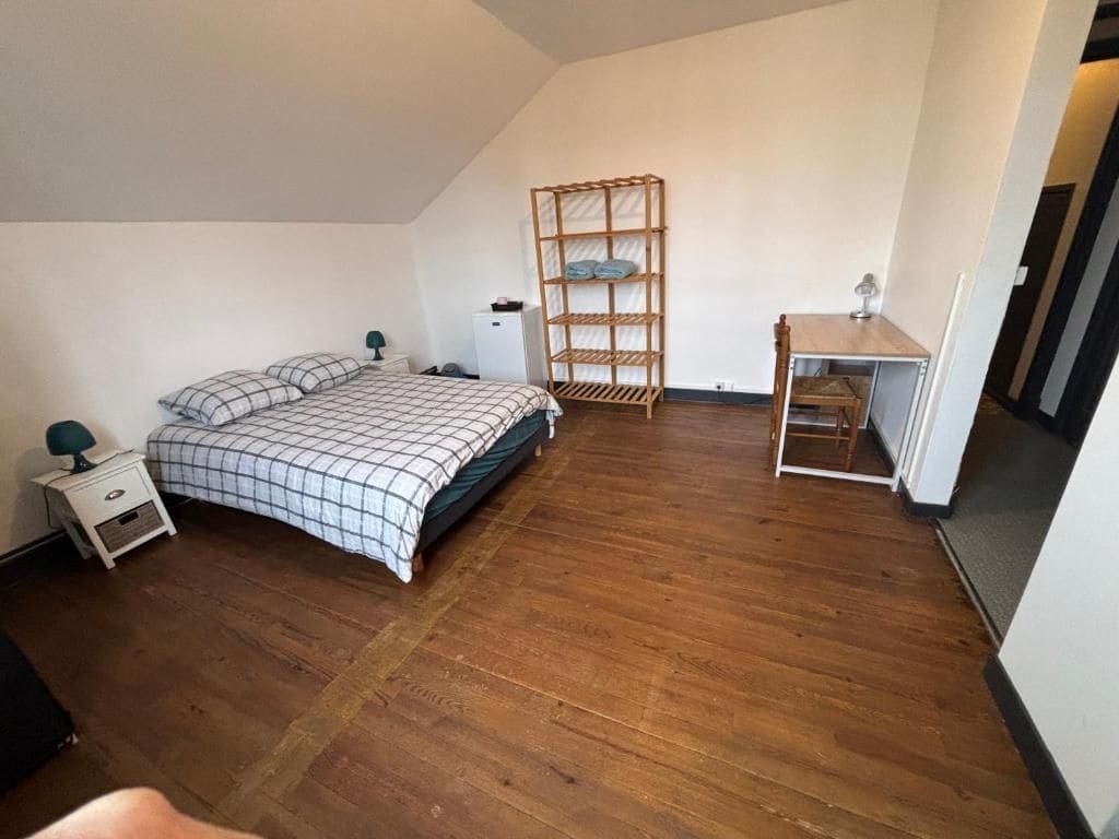 A bedroom with a bed, a wooden shelf unit, a desk, and a chair.