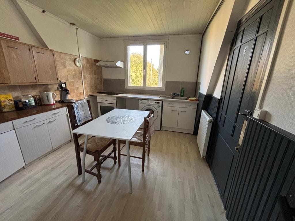 A compact kitchen with a dining table, wooden cabinets, a washing machine, and a window with a view.