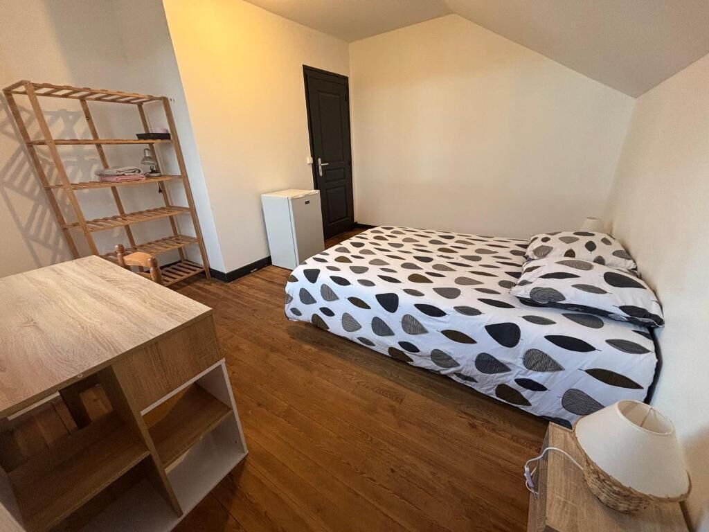 Un dormitorio con cama, escritorio de madera, calentador pequeño y una puerta.