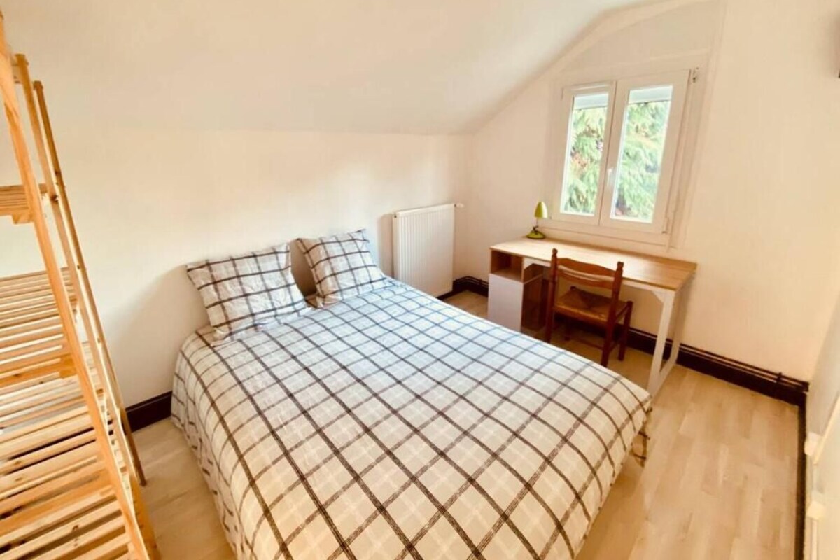 A bedroom with a bed, a desk, and a window.