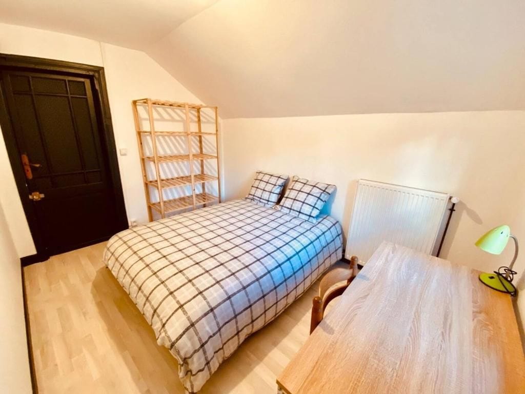 A bedroom with a bed, a wooden headboard, a bedside table, a lamp, and a radiator.