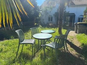A patio with four chairs and a table, surrounded by grass and a house with a tiled roof.