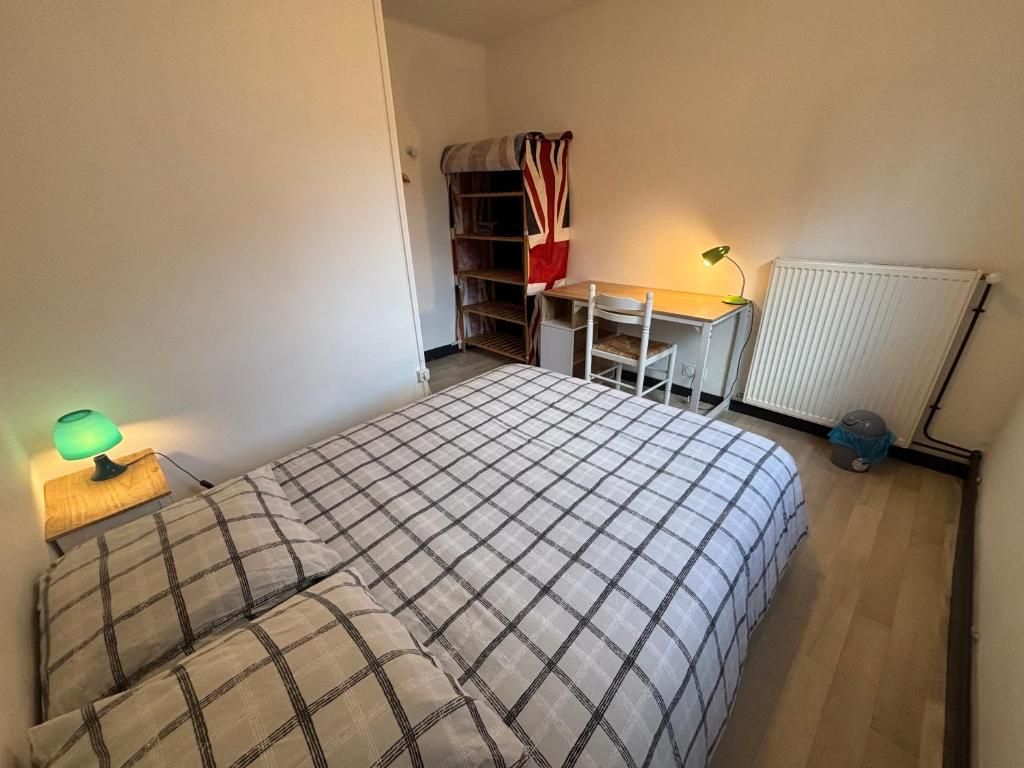 A bedroom with a bed, a desk, a chair, a radiator, and a shelf unit.