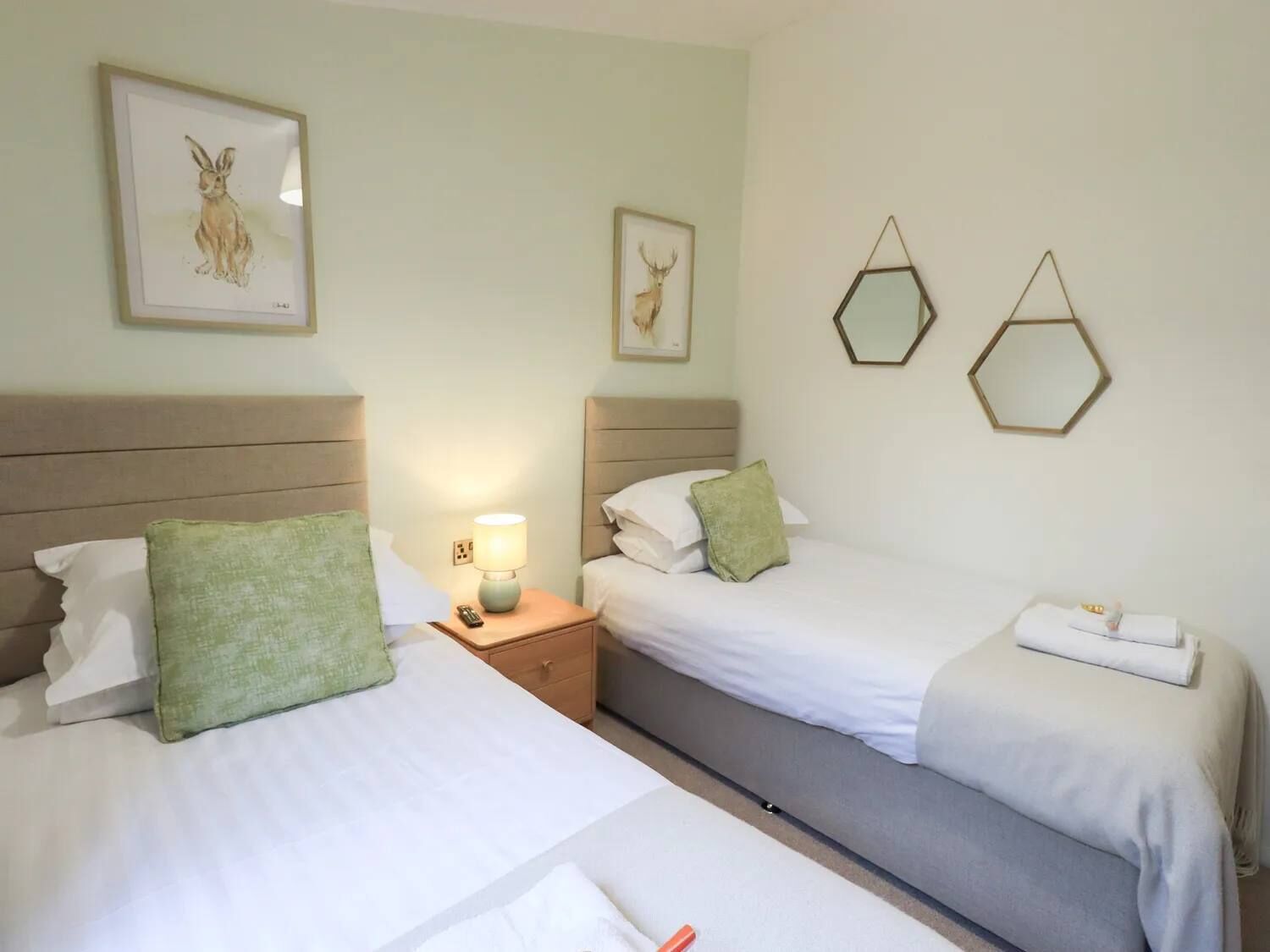 A hotel room with two beds, a nightstand with a lamp, and wall-mounted artwork.