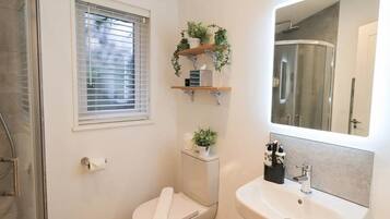 A bathroom with a toilet, sink, and shower. There are plants on a shelf above the toilet and a mirror above the sink.