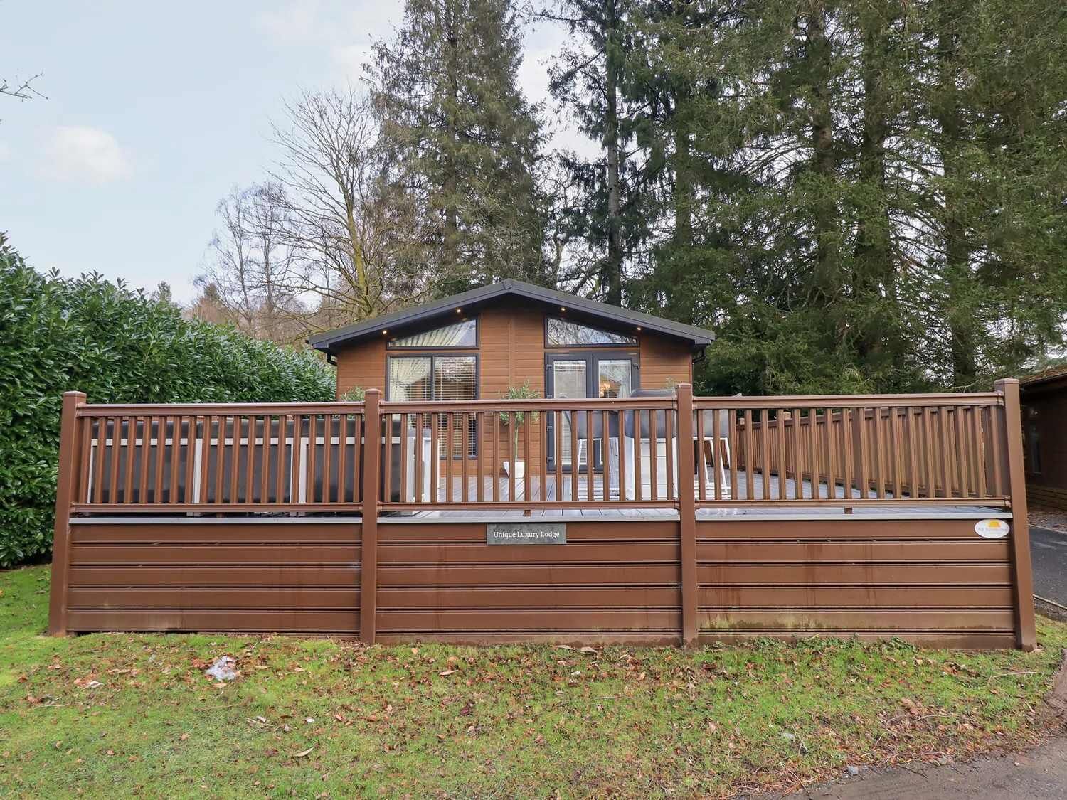 A lodge with a fenced deck area, a small building with a window, and a sign that reads 'Unique Luxury Lodge.'