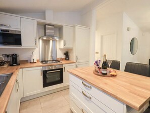 A modern kitchen with white cabinetry, a stainless steel range hood, a built-in oven, and a wooden countertop. - Luxury 2-Bed Lodge | White Cross Bay, Windermere (Westmorland and Furness)