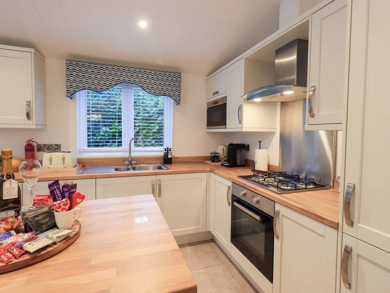 A modern kitchen with white cabinets, a stainless steel range hood, a gas stove, and a window with blinds.