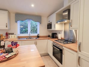 A modern kitchen with white cabinets, a stainless steel range hood, a gas stove, and a window with blinds. - Luxury 2-Bed Lodge | White Cross Bay, Windermere (Westmorland and Furness)