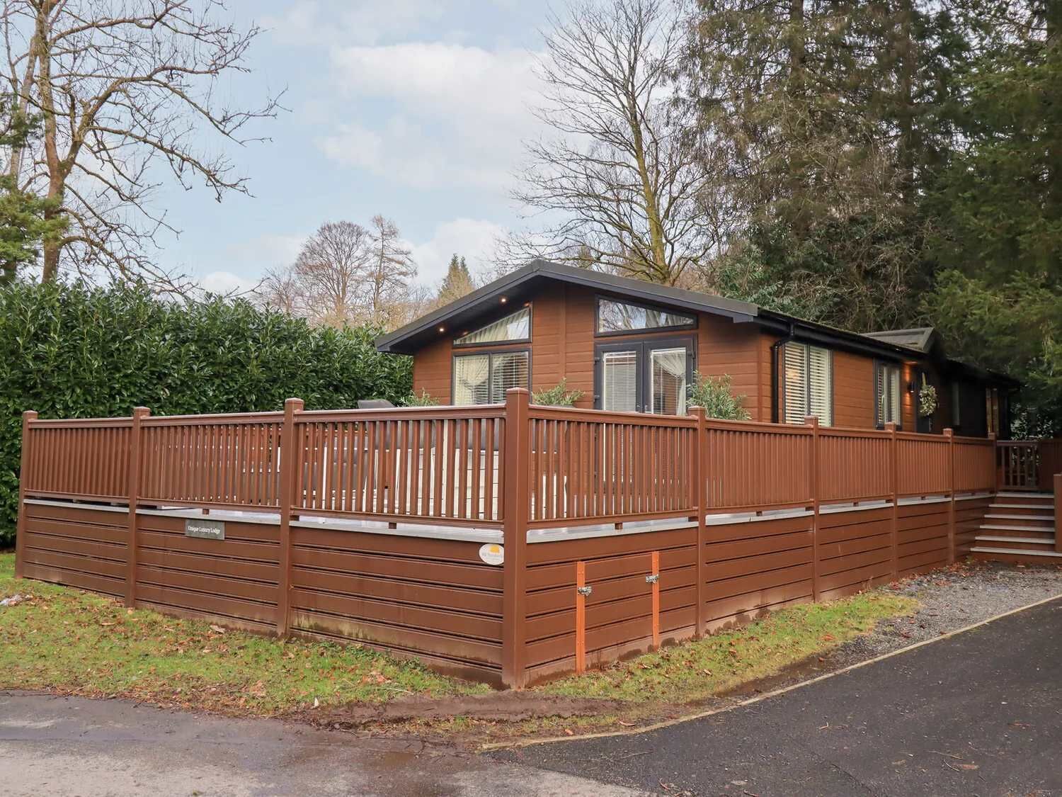 Ein eingeschossiges Holzhaus mit umzäunter Terrasse, kleiner Veranda und Garage.
