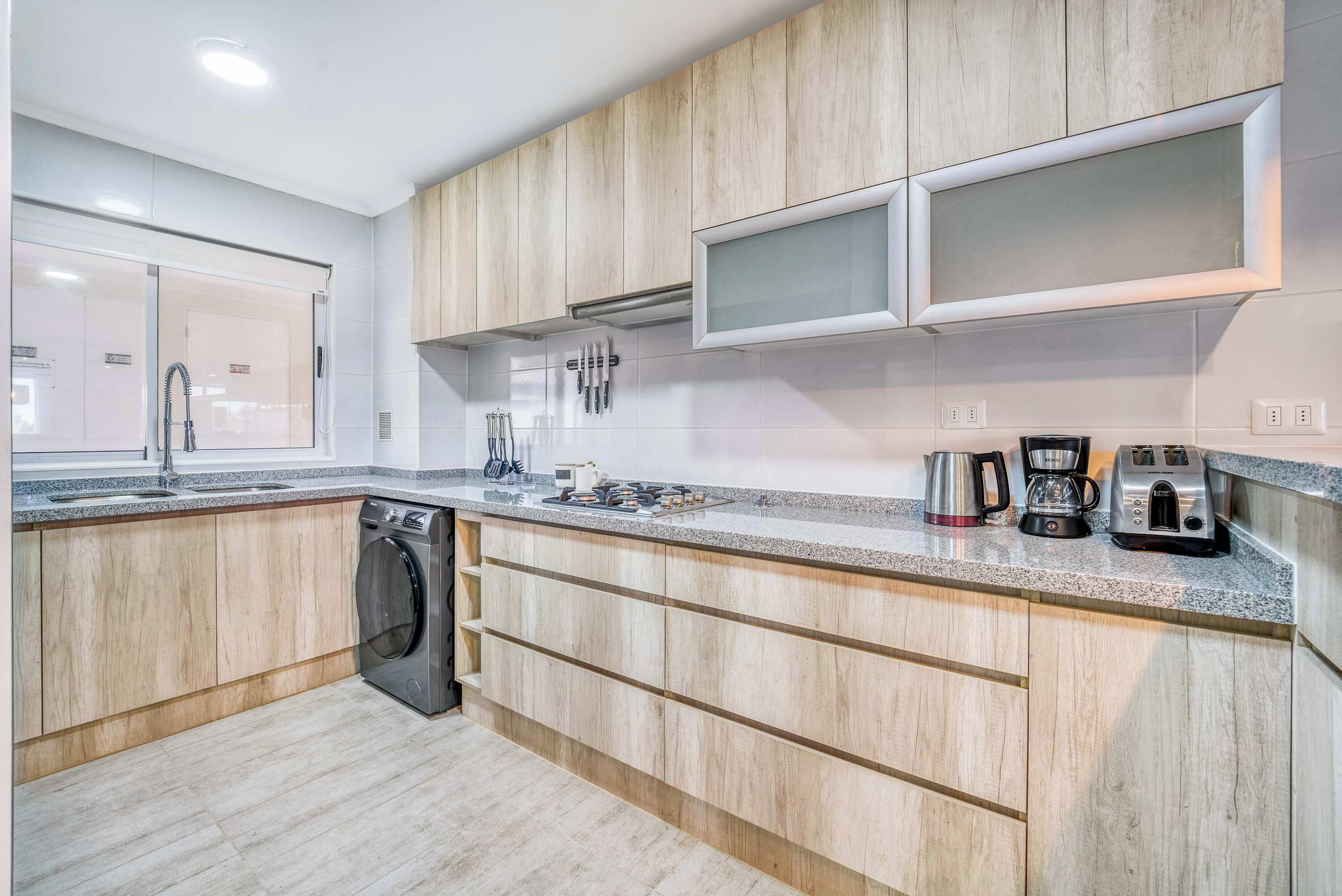 Une cuisine moderne avec des meubles en bois, un lave-vaisselle, une cuisinière et une machine à café.