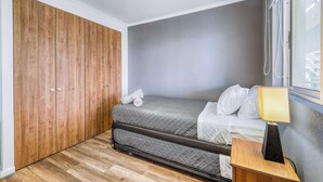 A compact bedroom with a bed, a nightstand, a window with blinds, and a wooden wardrobe. - Vista El Yeco | Vista al mar y acceso a playa (Algarrobo)