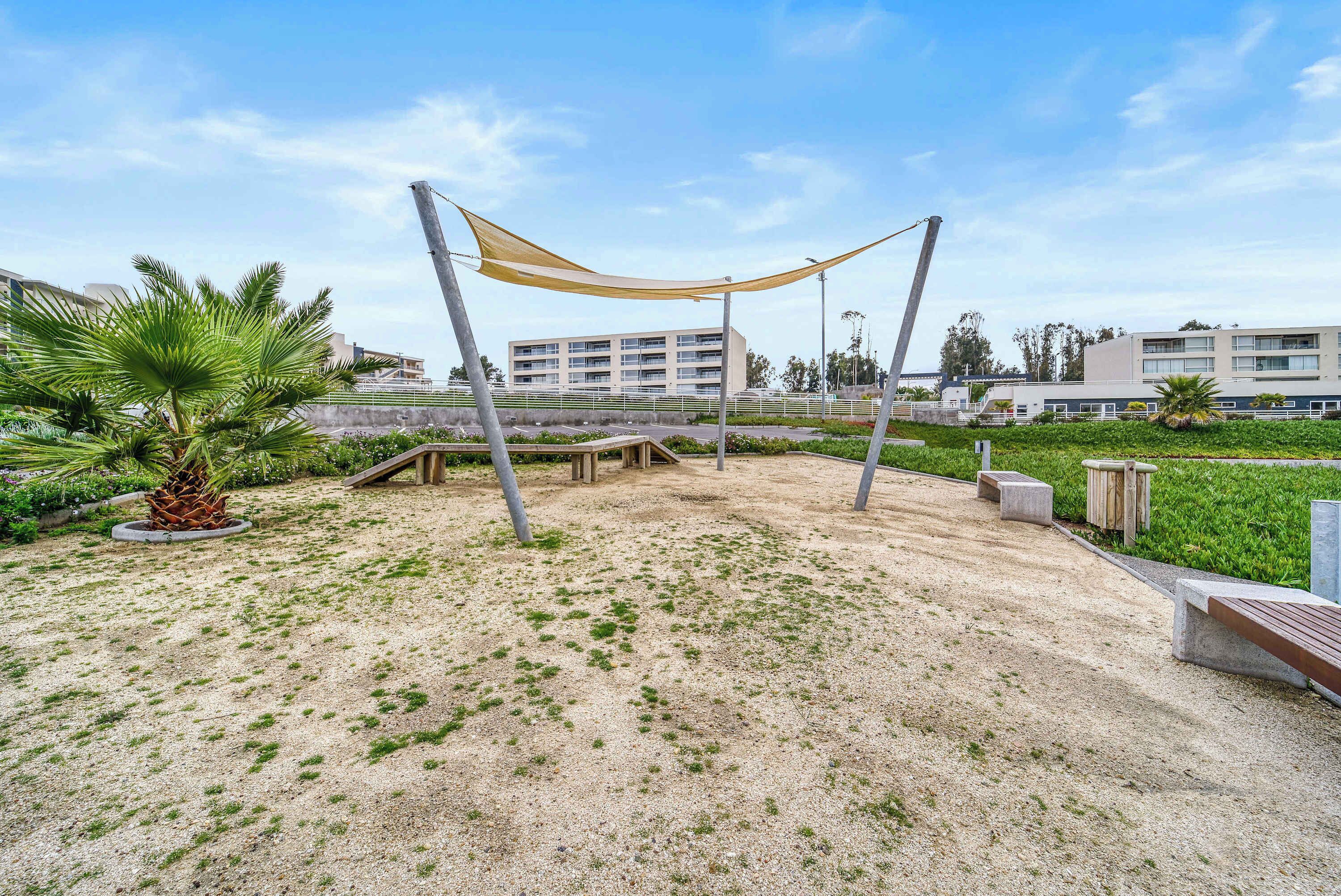 Um parque com uma área de estar arborizada, uma palmeira e um edifício ao fundo.