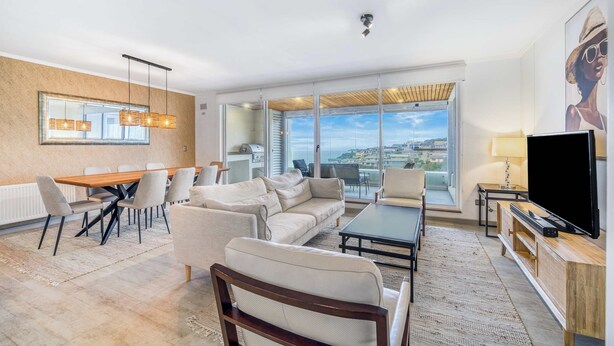 A modern living room with a dining area, a large window with a view, and a flat-screen TV. - Vista El Yeco | Vista al mar y acceso a playa (Algarrobo)