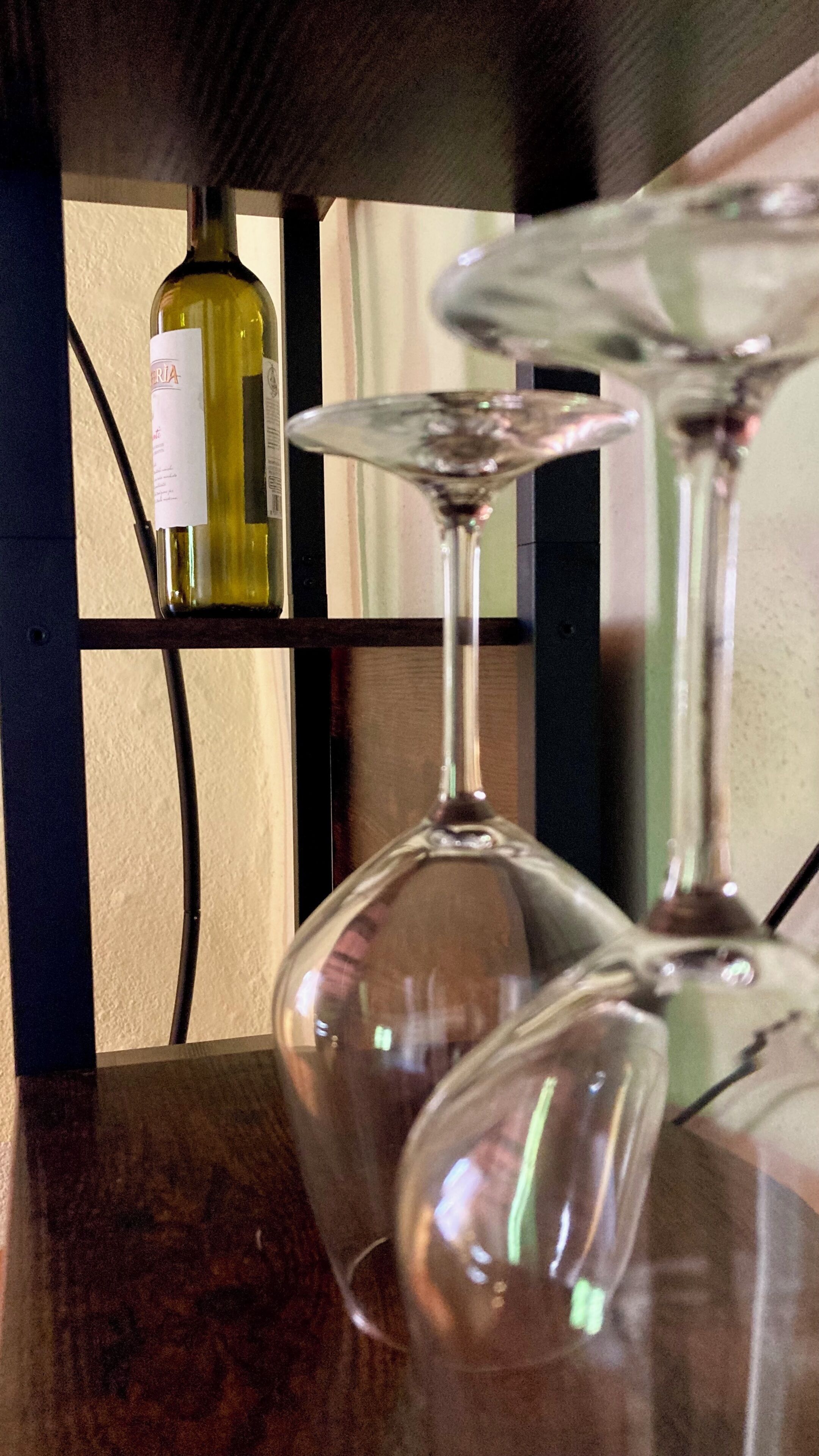 A glass wine bottle and two wine glasses on a shelf.