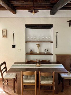 Ein Essbereich mit einem Holztisch, Stühlen und einem darüberliegenden Regal mit Weingläsern und einer Kaffeekanne.
