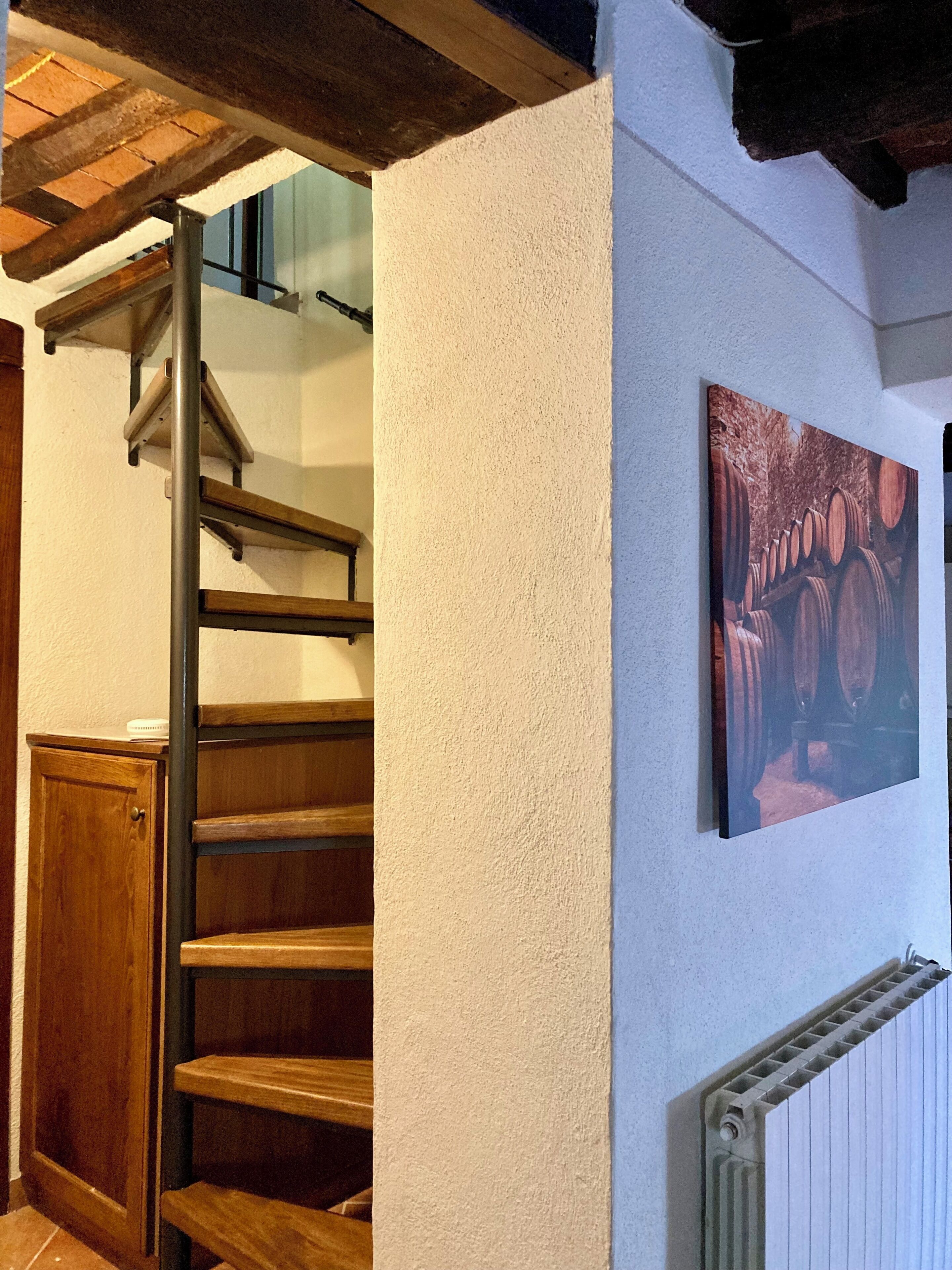 A staircase with wooden steps and a metal handrail, leading to a landing with a white wall and a framed picture of barrels.