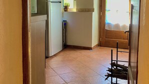 A narrow kitchen with a tiled floor, a refrigerator, a sink, and a window with a view of the outdoors.