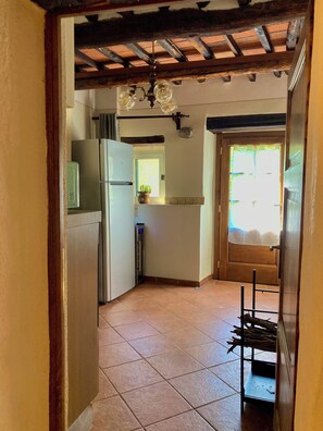 A narrow kitchen with a tiled floor, a refrigerator, a sink, and a window with a view of the outdoors.