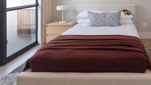 A bedroom with a bed, a nightstand, a lamp, and a window with blinds.