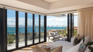 A spacious bedroom with a large bed, a view of the sea, and a balcony with outdoor seating.