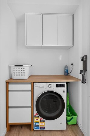 Ein kleiner Waschraum mit Waschmaschine, Wäscheständer und einem Schrank darüber.