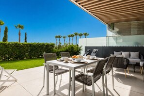 An outdoor patio with a dining table set for four, surrounded by chairs, and a sofa. - LOLA Beachfront Garden Apartment | Pools, Direct Beach Access, and Family-Friendly (Torremolinos)
