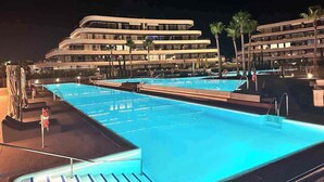 A swimming pool with a modern hotel building in the background. - LOLA Beachfront Garden Apartment | Pools, Direct Beach Access, and Family-Friendly (Torremolinos)